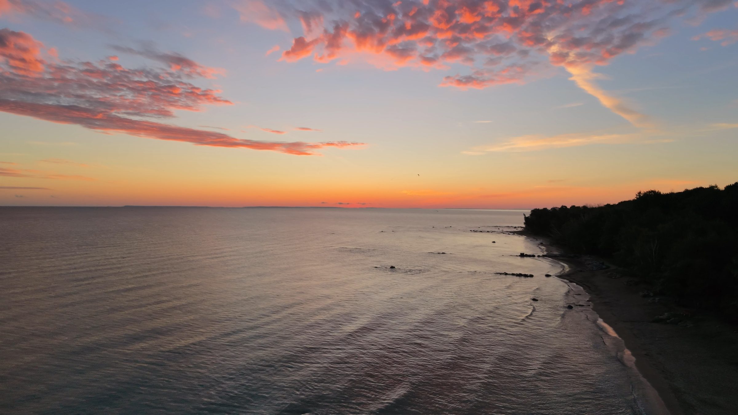 Pink clouds over still water and a forested point before sunrise